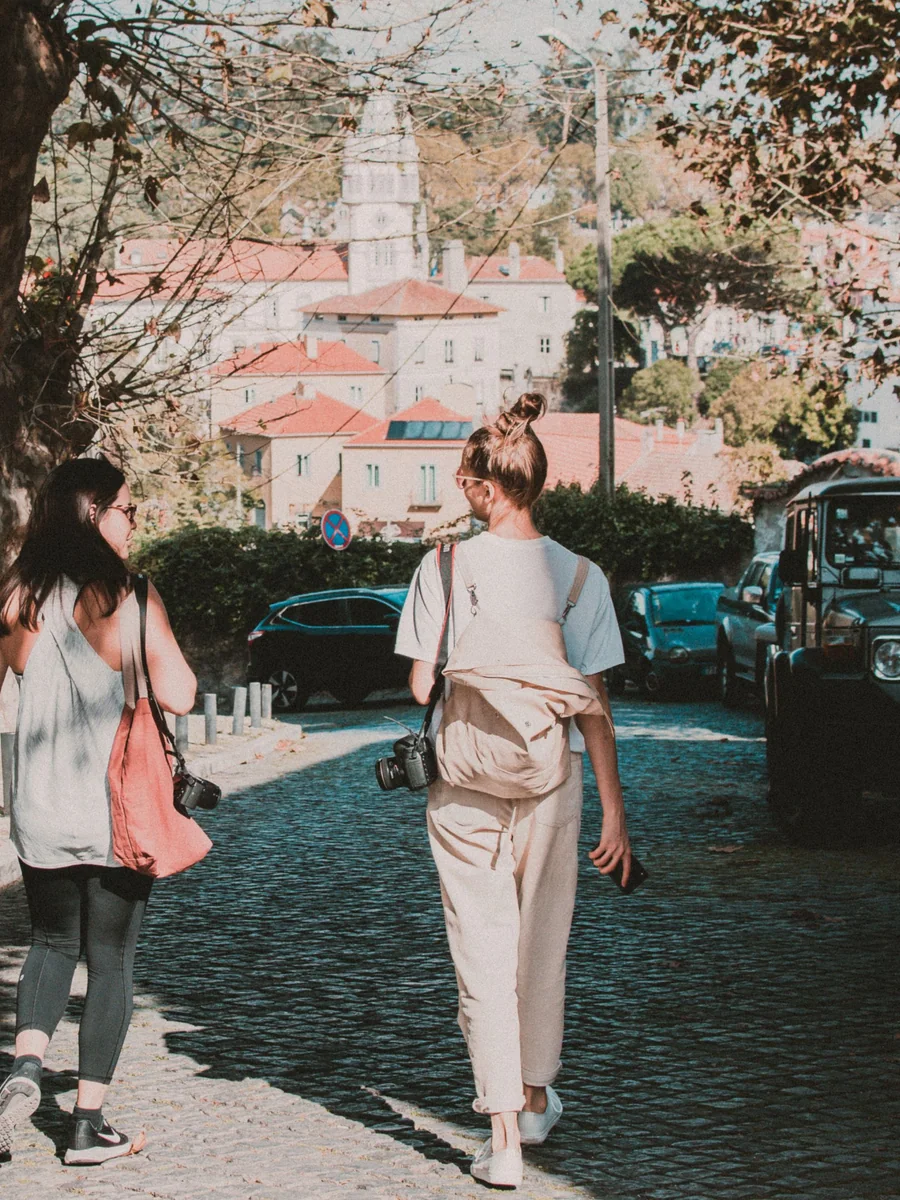 Two people walking together and photographing details along a tree-lined street.